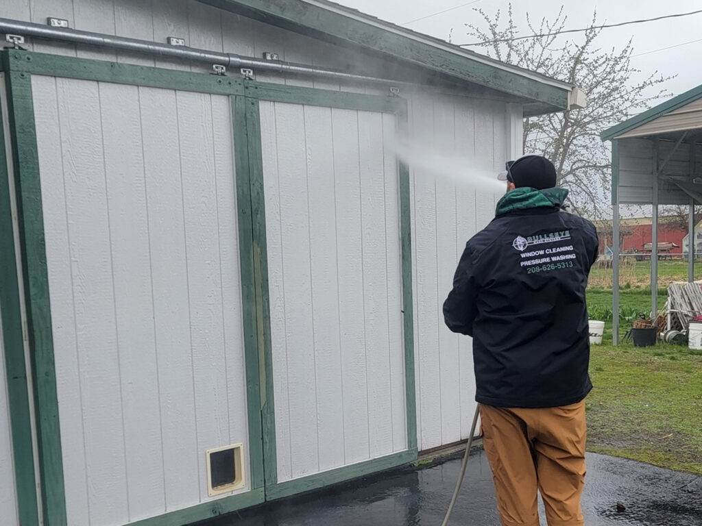 Pressure washing and soft washing exterior outbuilding on an acreage in Hauser, ID by Bullseye Wash Systems, removing dirt, mold, and grime.